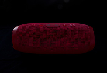 Wireless music speaker. Red bluetooth speaker on black background. Control and volume buttons.