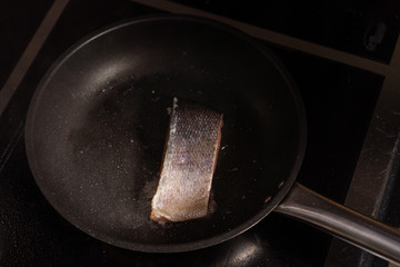 Chief is frying a piece of raw salmon on a pan in  a restaurant kitchen