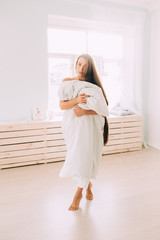 A beautiful long haired woman standing in white blanket in light room