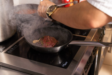 Frying a red meat steak on a pan with garlic and rosemary on a restaurant kitchen