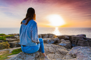 A girl sitting on a cliff watching Atlantic Ocean