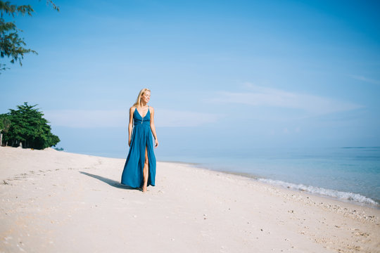 Sensual woman in blue dress walking on empty beach