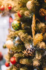 Red, golden and green balls and toys hanging on the fir tree. Festive mood. New year holidays decoration. Christmas concept. Selective focus, blurred background. Warm toned.