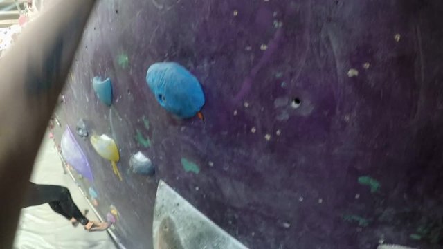 POV shot of tattooed young woman and brunette female companion bouldering together on artificial indoor wall at climbing gym and grabbing onto handholds of various shape and color, smeared with chalk