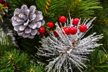 Close-up of the branches of an artificial Christmas tree with cones, red Holy berries, some of the...