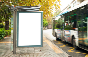 White blank vertical billboard at the bus stop on the city street. In the background of buses and...