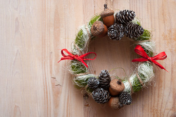 Christmas wreath with acorns, pine cones and red bows. On wooden background.