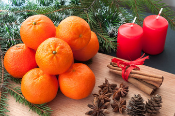 Christmas composition - candle, cones, orange, cinnamon, fir tree branch. On wooden background.