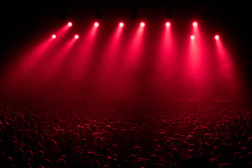 Red stage light with smoke in rock music concert. silhouettes of concert crowd in front of bright...