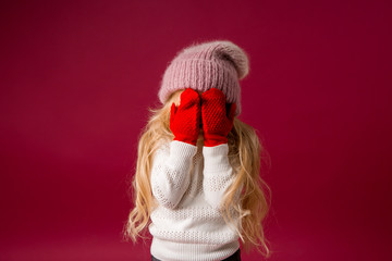 little blonde girl in a knitted hat and mittens smiles. winter clothes