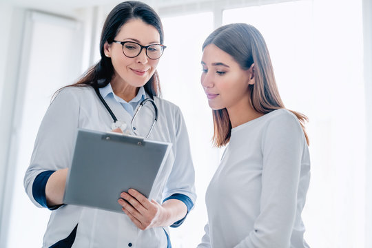 Smiling adult female doctor reporting medical results to young girl patient