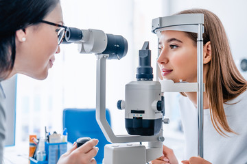 Side view shot of female doctor and patient in ophthalmology clinic - obrazy, fototapety, plakaty