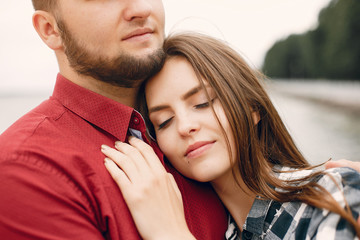 Cute couple in a park near river. Lady in a chirt. Guy in a red shirt