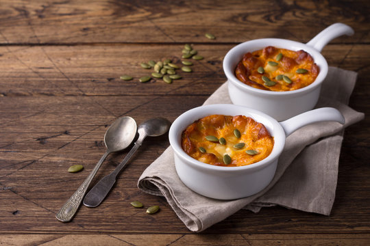 Pumpkin cheese casserole in ceramic mold with pumpkin seeds over wooden texture background, free space, horizontal
