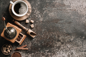 Coffee cup with coffee grinder and coffee beans on dark textured background.