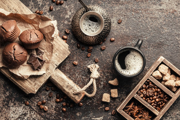 Coffee beans with coffee and muffins on dark textured background.