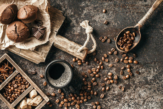 Coffee beans with coffee and muffins on dark textured background.