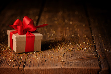 Gift box with red bow on rustic wooden table with golden glitter  -  Greeting card or gift coupon...