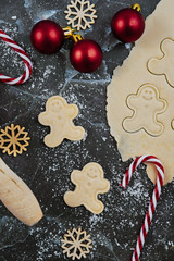 Overhead flat lay concept for baking Christmas cookies with rolled out cookie dough, cookies in the shape of happy gingerbread men ans seasonal decoration on dark marble background
