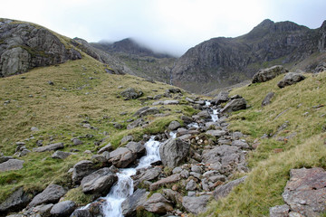 Fototapeta na wymiar Mountain stream leads up towards Clogwyn with Snowdon shrouded in cloud, Snowdonia National Park, North Wales