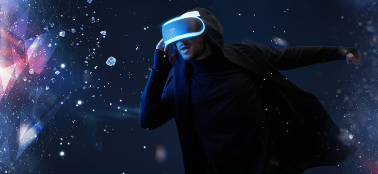 Young man having virtual reality experience. Guy using VR helmet. Dark magic universe background. Augmented reality, future technology, game concept.