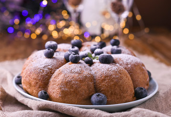 Christmas cake with berries and icing sugar on a wooden background. Traditional pastries in Italy. Bokeh on background
