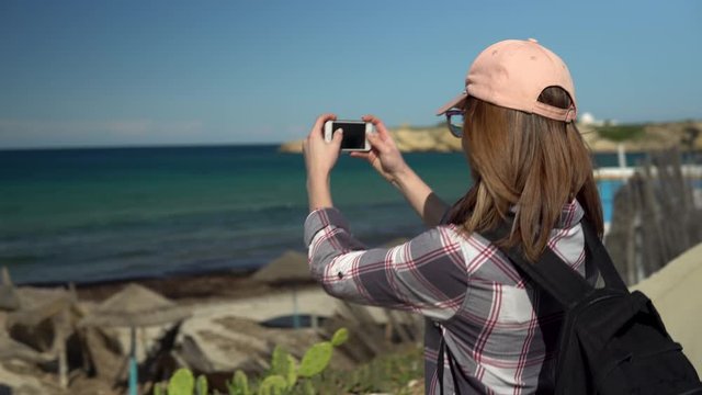 A young woman photographs the sea. A tourist backpacker photographs a beautiful view on the phone.