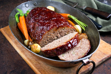 Traditional American meatloaf with ketchup from ground beef with carrots and onion as closeup in a copper saucepan
