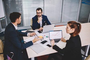 Owner of financial company talking with business partners about developing new project during brainstorming in office sitting at meeting table with laptops.Proud ceo discussing plan with colleagues