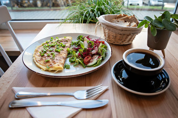 Healthy vegetarian food for breakfast. Omelette with salad, bread and black coffee on a table in restaurant. Close up.