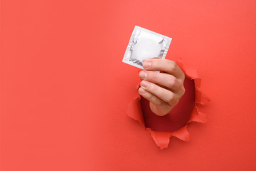 Hand give condom on torn red paper wall. Safe pleasure and protection, contraception, protection from AIDS and day to fight AIDS. Copy space aside for your advertising content - obrazy, fototapety, plakaty