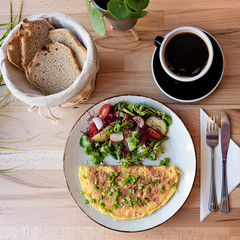 Omelette with salad on a plate with black coffee for breakfast on a wooden table in restaurant. Tasty vegetarian food.
