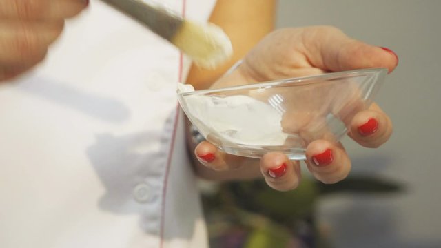 The process of preparing facial mask. Glass bowl in the hands of a beautician