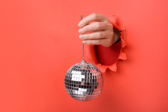 Hand holding Silver disco mirror ball on torn red paper wall. Copy space aside for your advertising and offer or sale content.