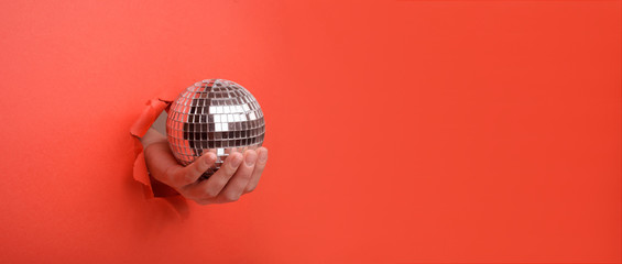 Hand holding Silver disco mirror ball on torn red paper wall. Copy space aside for your advertising...