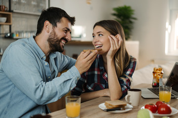 Fototapeta na wymiar Happy woman being fed by her boyfriend during breakfast time at home