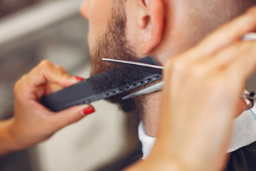 Man with a beard. Hairdresser with a client. Woman with scissors and a comb