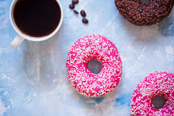Tasty and delicious donuts with pink icing and powder, with chocolate icing, with a cup of aromatic coffee on a blue concrete background.