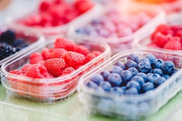 Plastic boxes with raspberries, blueberries, blackberries on counter of market store
