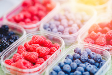 Plastic boxes with raspberries, blueberries, blackberries on counter of market store