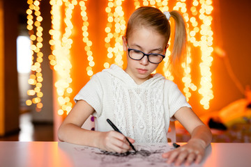 Adorable litle girl is writting a letter to Santa Klaus sitting on the table
