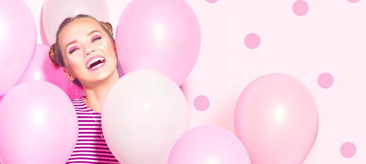 Fototapeta na wymiar Beauty girl with colorful air balloons laughing over pink background. Beautiful Happy Young woman on birthday holiday party. Joyful model having fun, playing and celebrating with pastel color balloon