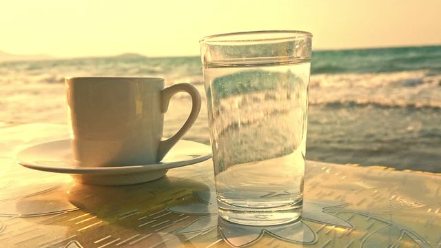 Turkish coffee and glass of water front of slow motion sea wave.