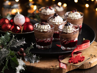 Dessert in a glasses with chocolate and berries spread on wooden background with garland lights bokeh and christmas decoration. New year holidays background concept. Dessert recipe ideas.
