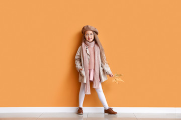 Fashionable little girl in autumn clothes near color wall