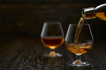 Pouring cognac from the bottle into the glass against wooden background.