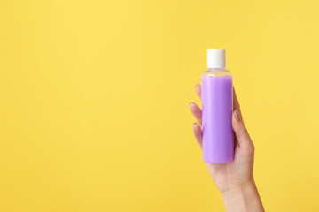 Female hand with cosmetic product in bottle on color background