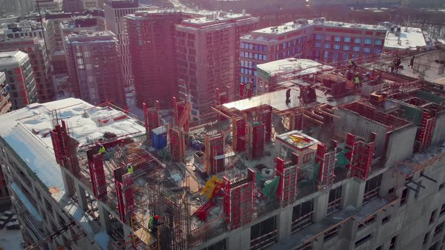 Picturesque aerial view to the construction works on the top of a skyscraper on a sunny winter day. Giant cranes, workers, empty window holes of a new building and Moscow City Center on the background