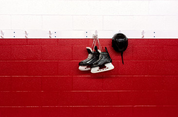 Hockey skates hanging in locker room with helmet over red background with copy space
