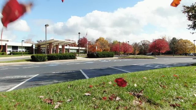 Aerial, low approach colorful autumn leaves blow up in front of the camera as it approaches Kissel Hill  Elementary School, Lititz, Lancaster County, Pennsylvania.
